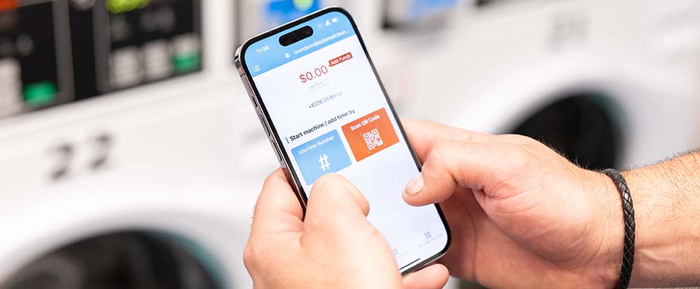 Two hands hold a phone showing a page of Automatic Laundry's Laundry 101 app