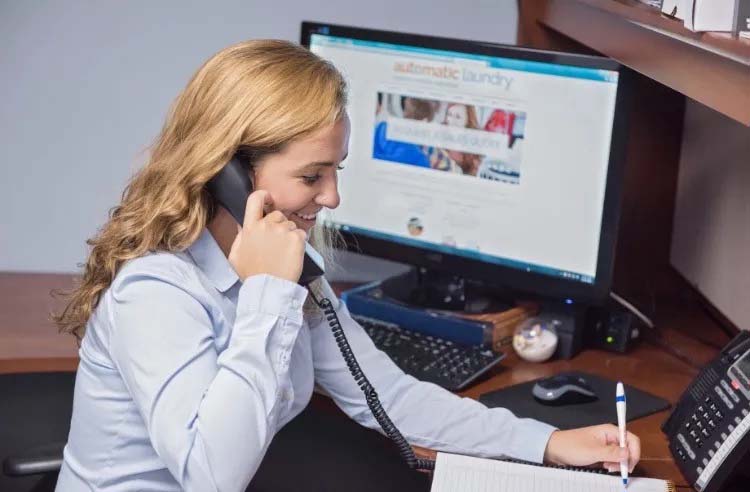 A woman taking a phone call from a work desk while writing something down