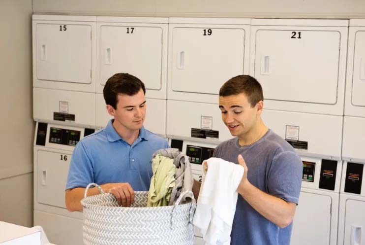 Two young men folding laundry in a laundry room