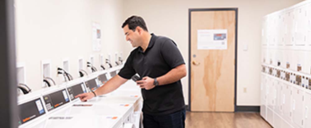 A man reaches to press a button on a laundry machine in a laundry room
