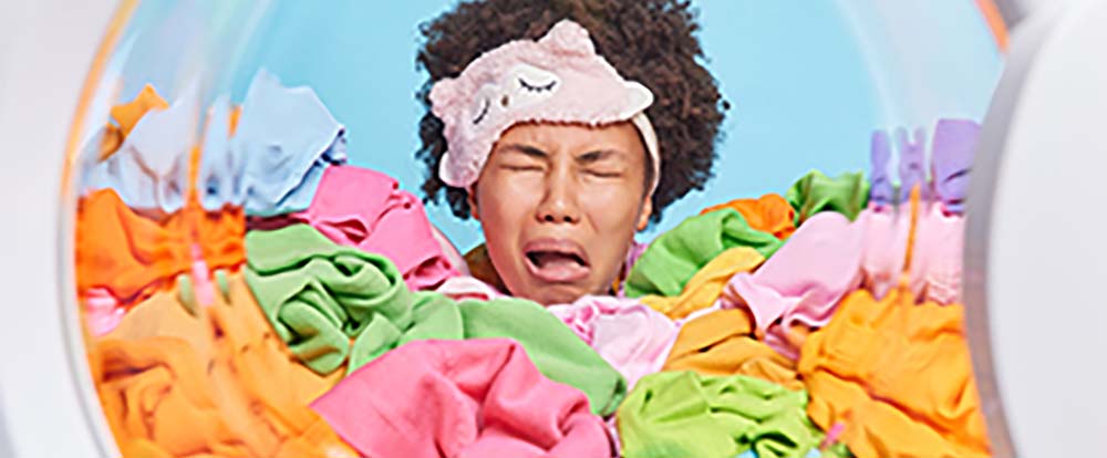 A woman has a negative facial expression while clothes are being washed in a laundry machine
