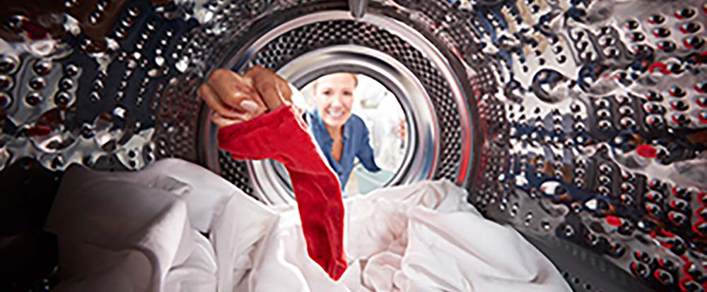 A woman getting started with laundry by putting a red sock into a laundry machine
