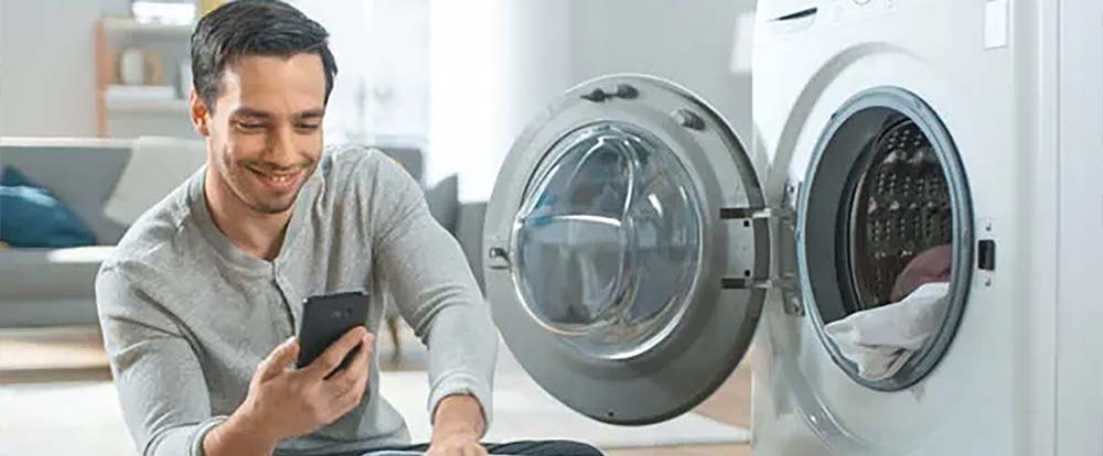 A man in front of an open laundry machine, using his phone to learn how to use the machines