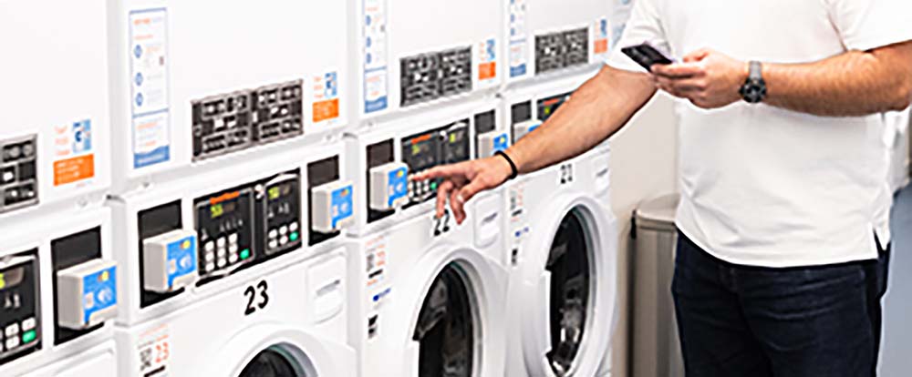 A man's arm reaching to press a button on an Automatic Laundry machine