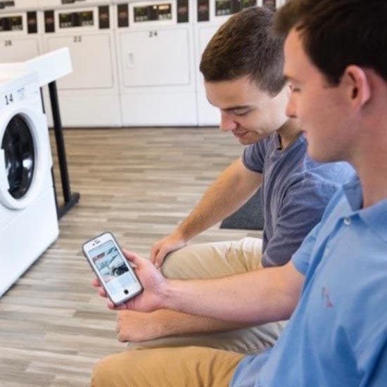 Two men sitting in a laundry room looking at a phone