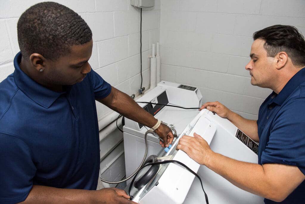 Two service technicians working on a laundry machine for their careers with Automatic Laundry