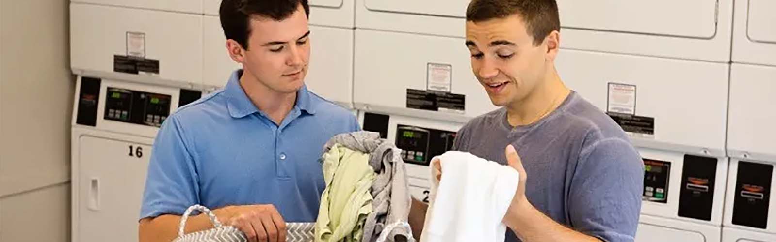 Two young men folding laundry in a laundry room