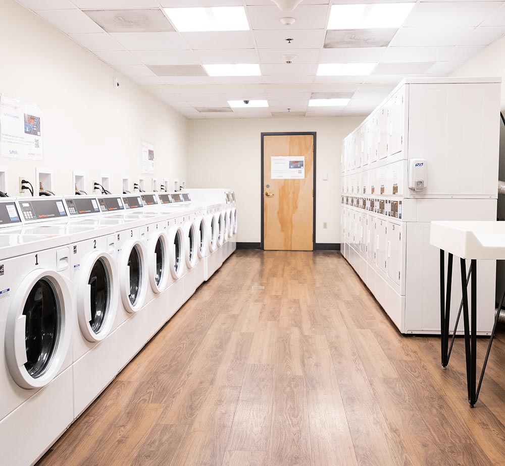 Full service laundry room with commercial washers & dryers on each side and a door in the middle